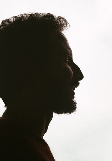 Silhueta de perfil de um homem com cabelo encaracolado e barba a sorrir.